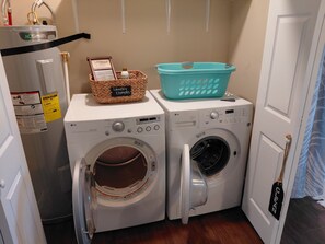 A laundry room with two washing machines, a basket labeled 'Laundry Essentials,' and a water heater.