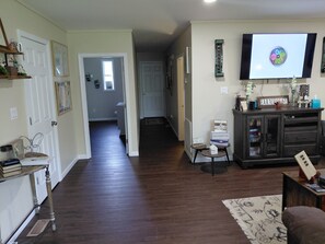 A living room with a dark wood floor, a television mounted on the wall, a cabinet with decorative items, and a rug.