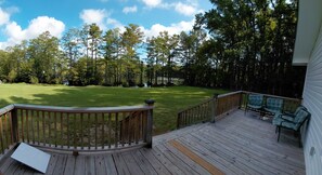 A deck with a view of a grassy yard and trees.