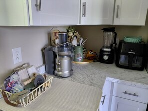A kitchen with white cabinets, a blender, a coffee maker, and a basket with cleaning supplies.