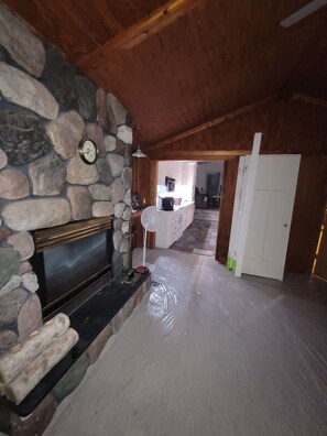 A room with a stone fireplace, a fan, and a partially covered floor.