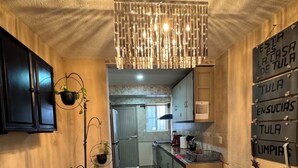 A narrow hallway with a kitchen area on the right, featuring cabinets, a countertop, and a hanging light fixture. - Orchid House (Cancún)