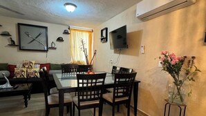 A dining area with a table and chairs, a television mounted on the wall, and a decorative vase with flowers. - Orchid House (Cancún)