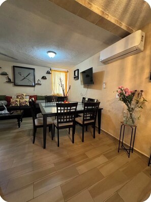 Ein Essbereich mit Tisch und Stühlen, einem an der Wand befestigten Fernseher und einer dekorativen Vase mit Blumen.