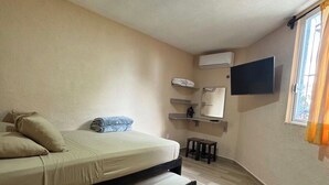 A bedroom with a bed, a flat-screen TV mounted on the wall, an air conditioning unit, and a window with curtains. - Orchid House (Cancún)