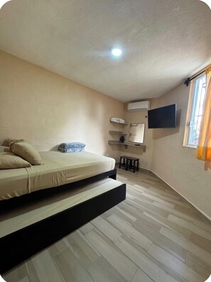 Ein Schlafzimmer mit einem Bett, einem flachbildfernseher an der Wand, einer Klimaanlage und einem Fenster mit Vorhängen.