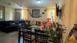 A dining area with a table and chairs, a clock on the wall, and a vase with flowers. - Orchid House (Cancún)