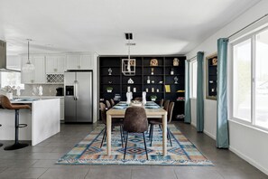 Eine moderne Küche mit weißen Schränken, einem Edelstahlkühlschrank und einem Essbereich mit Holztisch und -stühlen.