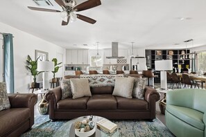A modern living room with a brown leather sofa, a coffee table, and a dining area with a chandelier. - The ONLY FREE-Heated Pool + Hot Tub + Game Lounge Combo — 10 Min to Old Town (Scottsdale)