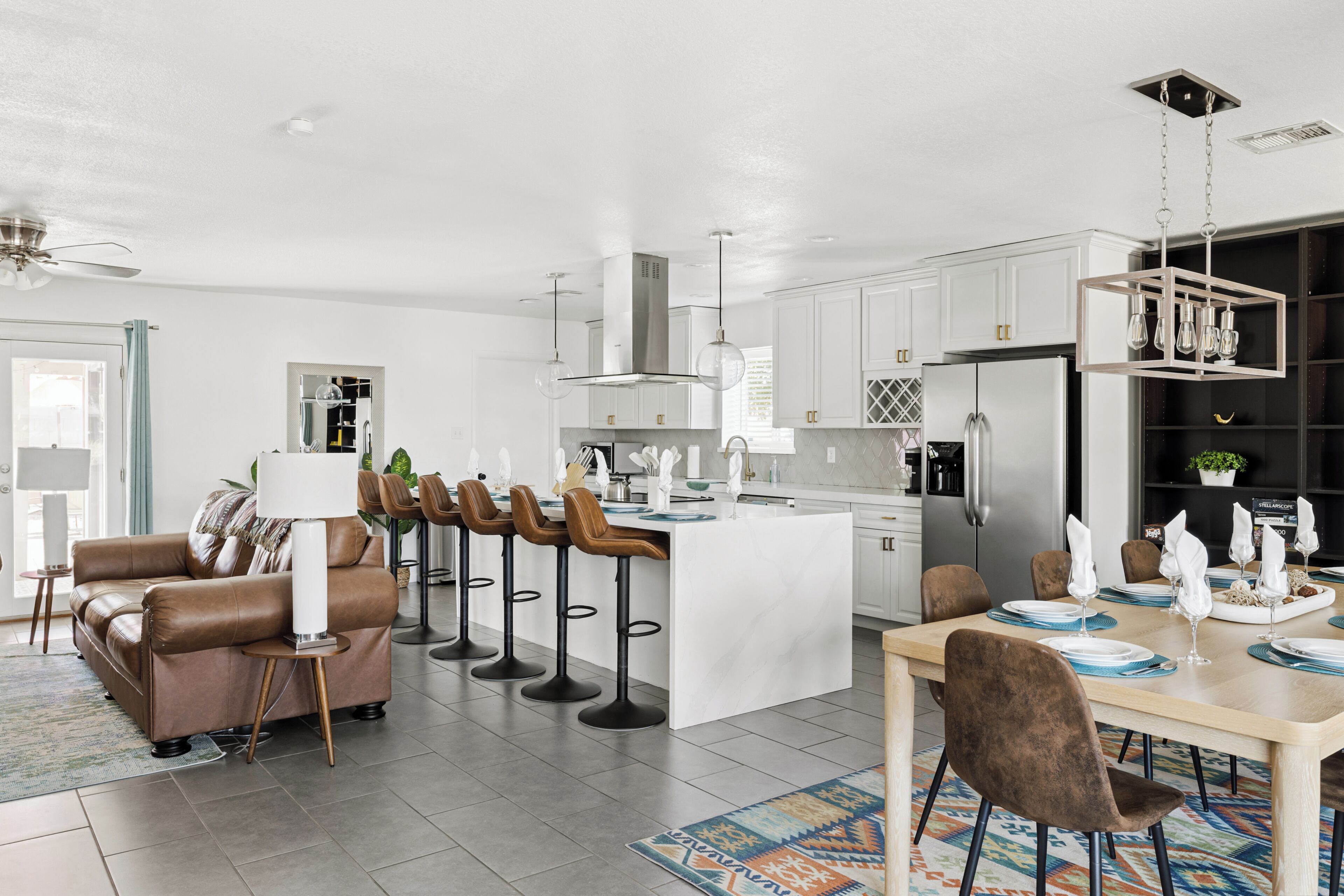 A modern kitchen with white cabinets, a stainless steel refrigerator, and a dining area with a wooden table and bar stools.