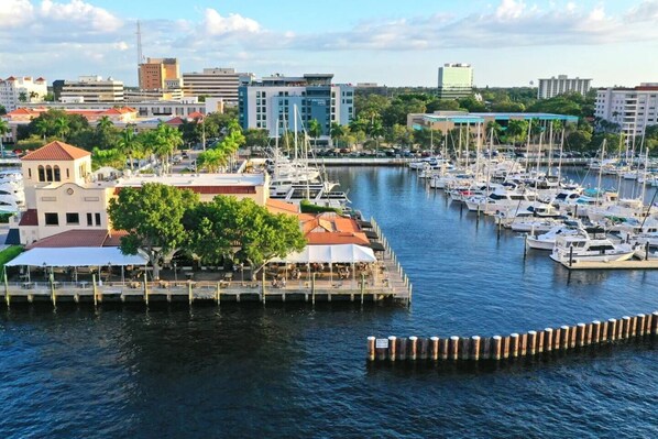 Marina con varias embarcaciones amarradas, un restaurante frente al agua y edificios circundantes.