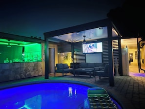 A pool area with a bar and seating, a television screen, and a ceiling fan. - West Tampa Villas # 3 Near Stadium & Airport And Pool (Tampa)