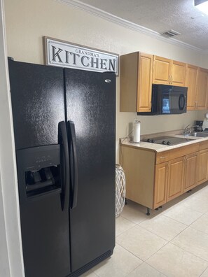 A kitchen with a black refrigerator, wooden cabinets, a microwave, and a coffee maker. - West Tampa Villas # 3 Near Stadium & Airport And Pool (Tampa)