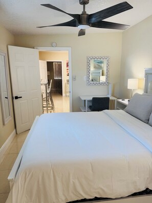 A hotel room with a bed, a desk, a chair, a desk lamp, a ceiling fan, and a door leading to a balcony. - West Tampa Villas # 3 Near Stadium & Airport And Pool (Tampa)