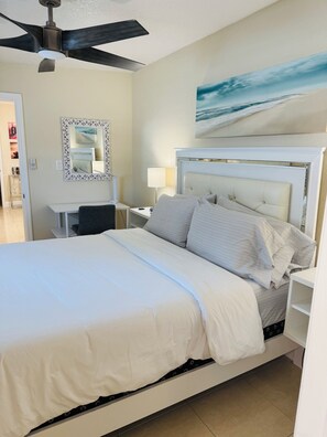 A hotel room with a bed, a nightstand, a lamp, a ceiling fan, a wall-mounted mirror, and a painting of a beach scene. - West Tampa Villas # 3 Near Stadium & Airport And Pool (Tampa)