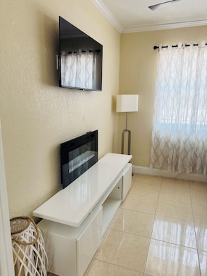 A room with a flat-screen TV mounted on the wall, a white console table, a lamp, and a patterned curtain. - West Tampa Villas # 3 Near Stadium & Airport And Pool (Tampa)