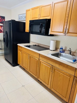 A kitchen with wooden cabinets, a black refrigerator, a microwave, a sink, and a countertop. - West Tampa Villas # 3 Near Stadium & Airport And Pool (Tampa)