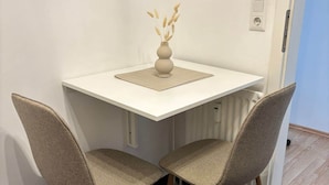 A small dining area with a white table, two chairs, and a vase with dried plants. - Modern studio in a central location (Salzgitter)