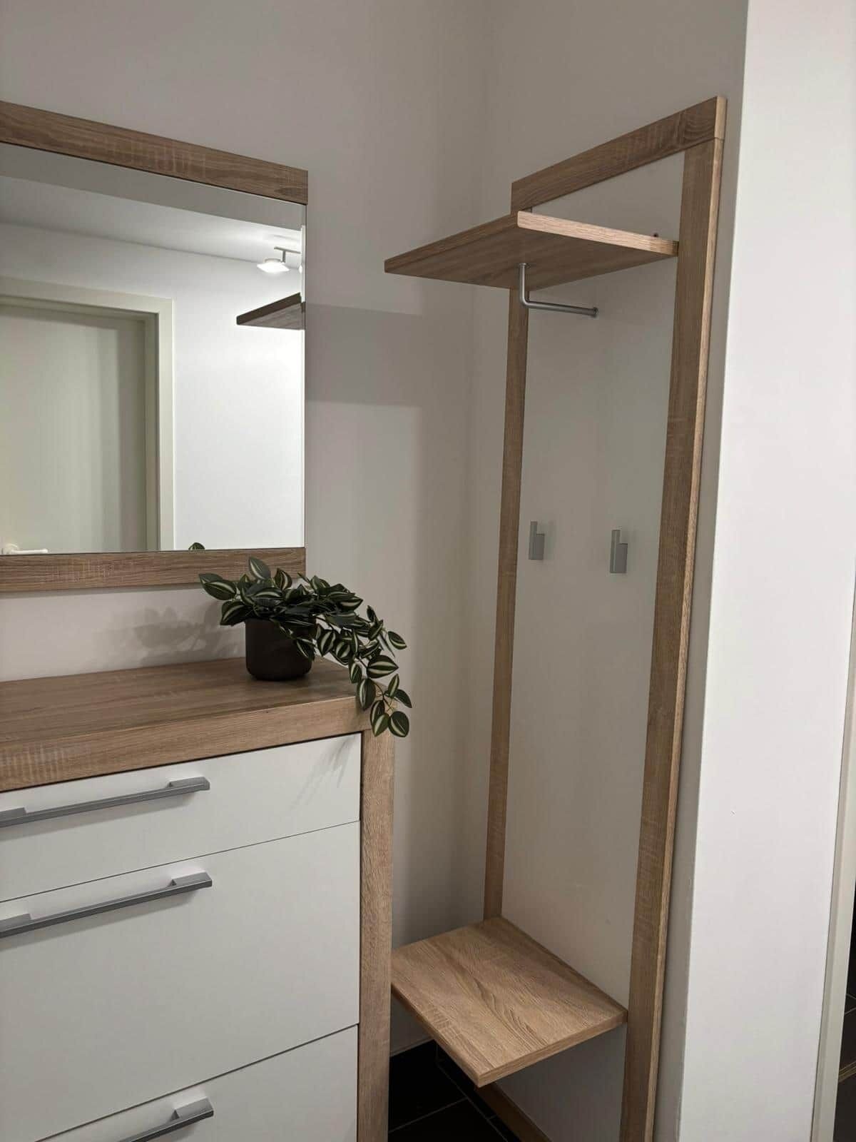 Une salle de bain avec un meuble-lavabo en bois, un miroir, une plante en pot et une étagère verticale.