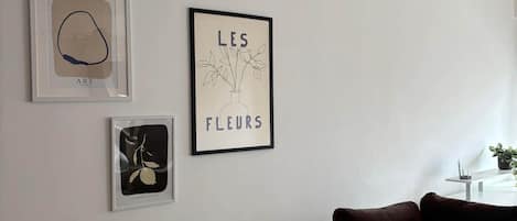 A living room with a beige sofa, two framed artworks, and a small table with a plant.