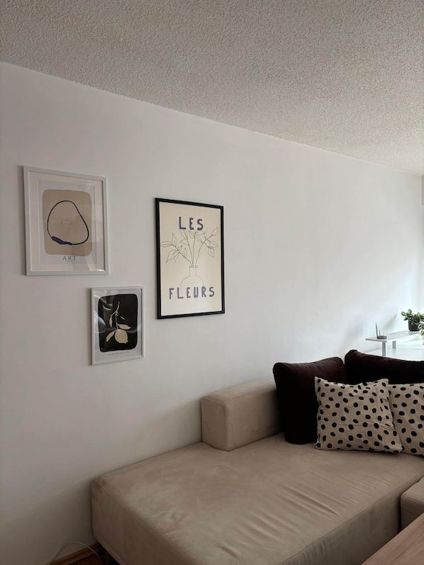 A living room with a beige sofa, two framed artworks, and a small table with a plant.