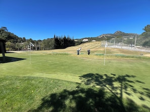 A golf course with a clear sky, a well-maintained green, and a distant mountain.