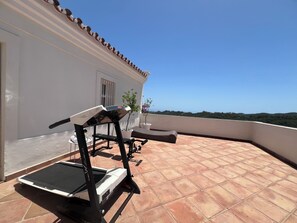A balcony with a treadmill, a potted plant, and a view of the landscape.