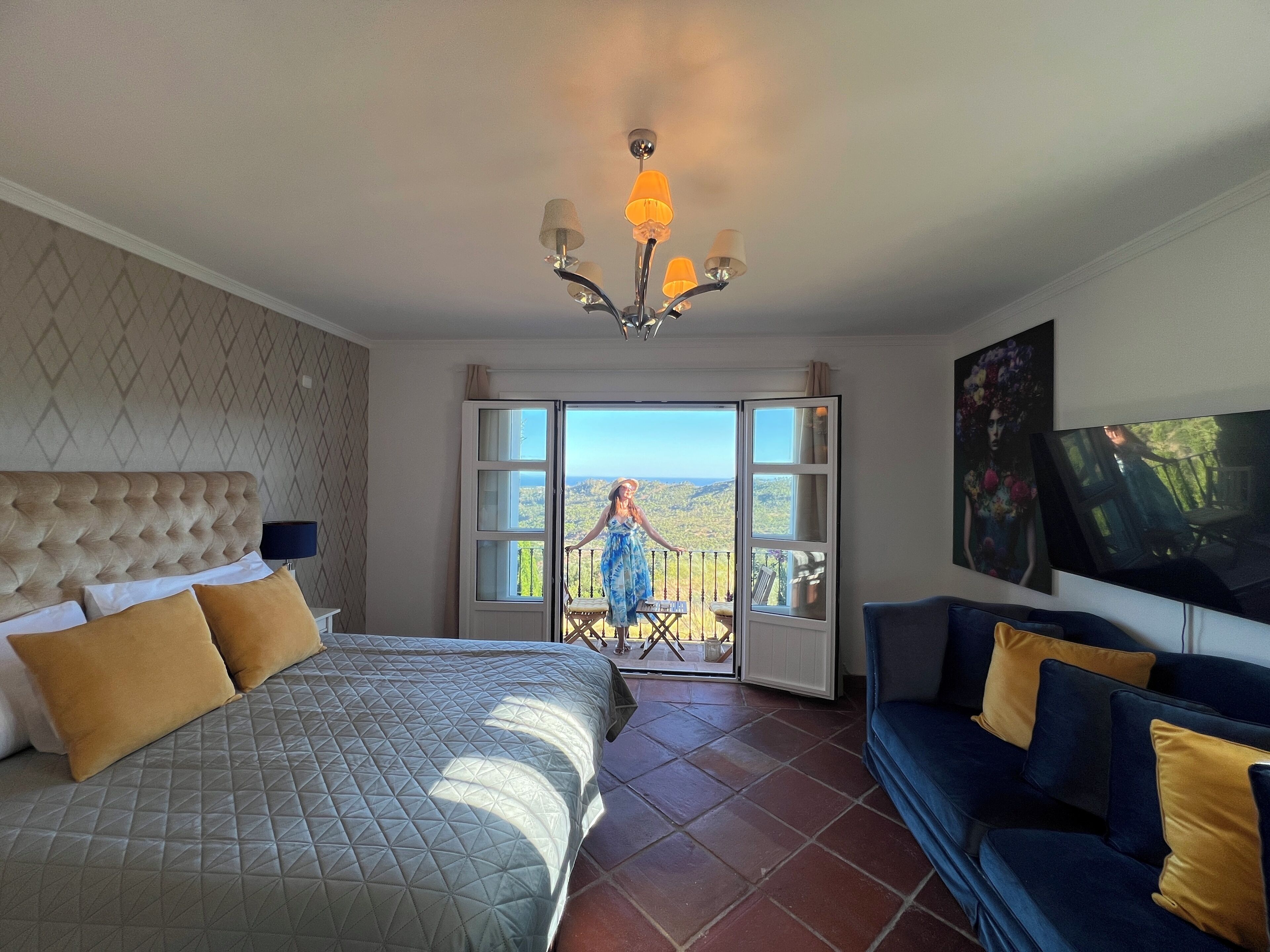 A bedroom with a bed, a sofa, a TV, and a balcony with a view.