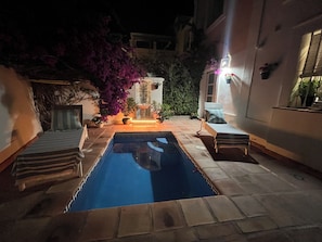 A swimming pool with a tiled deck, surrounded by potted plants and a small fountain.