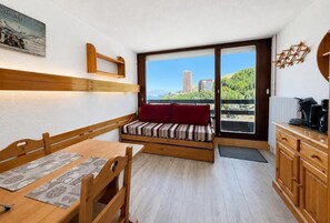 Ein kleines Zimmer mit einer hölzernen Bank, einem Esstisch und Blick auf ein Gebäude durch eine Glastür.