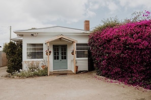 A single-story house with a front porch, a chimney, and a garden with pink flowers. - Whimsy Cottage | Kingston Beach Retreat with Outdoor Bath (Kingston Beach)