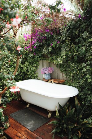 Eine weiße, freistehende Badewanne in üppiger Gartenlandschaft.