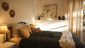 Un dormitorio con cama, lámparas de noche, un cuadro floral y una ventana con cortinas.