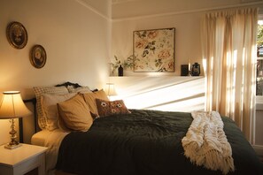 Ein Schlafzimmer mit einem Bett, Nachttischlampen, einem Blumenbild und einem Fenster mit Vorhängen.