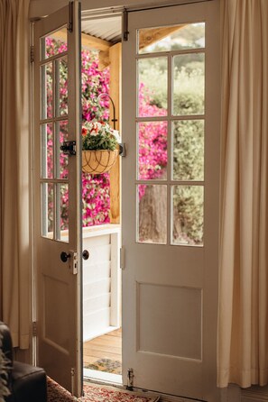 A wooden door with a view of a balcony and pink flowers. - Whimsy Cottage | Kingston Beach Retreat with Outdoor Bath (Kingston Beach)
