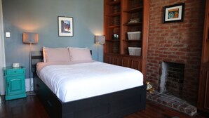 A bedroom with a bed, a nightstand, a dresser, a brick fireplace, and a framed picture on the wall. - Historic 1 Bedroom Apartment in Marigny Neighborhood next to French Quarter (New Orleans)