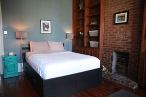 A bedroom with a bed, a nightstand, a dresser, a brick fireplace, and a framed picture on the wall. - Historic 1 Bedroom Apartment in Marigny Neighborhood next to French Quarter (New Orleans)