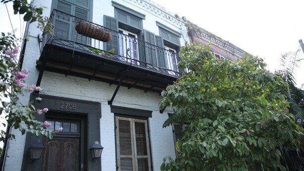 A two-story building with a balcony, a wooden door, and a window with shutters. - Historic 1 Bedroom Apartment in Marigny Neighborhood next to French Quarter (New Orleans)