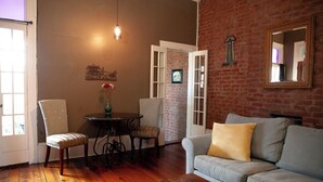 A room with a brick wall, a sofa, a table with chairs, and a hanging light fixture. - Historic 1 Bedroom Apartment in Marigny Neighborhood next to French Quarter (New Orleans)