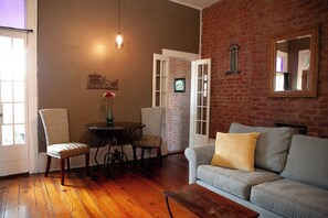 A room with a brick wall, a sofa, a table with chairs, and a hanging light fixture. - Historic 1 Bedroom Apartment in Marigny Neighborhood next to French Quarter (New Orleans)