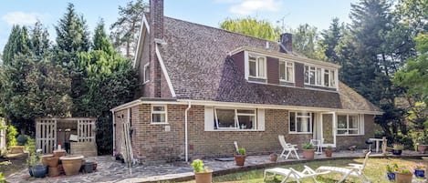 A two-story house with a sloped roof, brick exterior, and a front porch with white chairs.