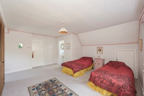 Een slaapkamer met twee eenpersoonsbedden, een klein nachtkastje, een hanglamp en een kamerbreed tapijt met dessin.