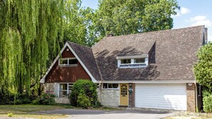 Ett tvåvåningshus med ett sluttande tak, ett garage och en trädgård framför huset.