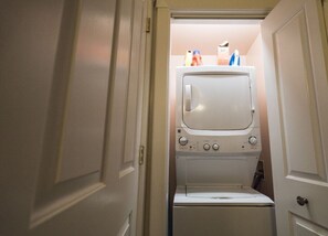 Une buanderie équipée d’un lave-linge et d’un sèche-linge superposés, d’une porte et d’une étagère contenant des produits de nettoyage.