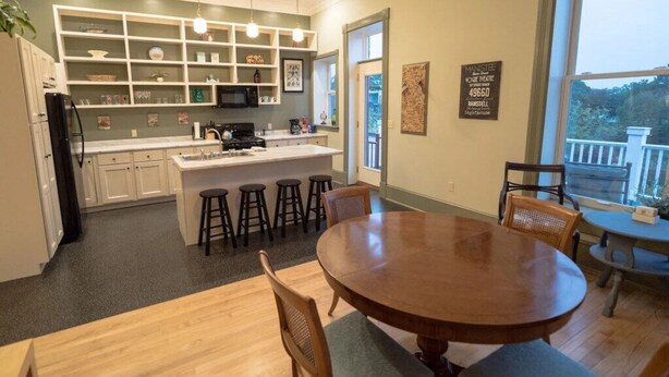 Una cocina con una isla central, taburetes de bar, una mesa de comedor y vistas al exterior.