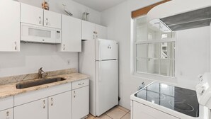 A modern kitchen with white cabinets, a stainless steel sink, a microwave, a refrigerator, and a stove.