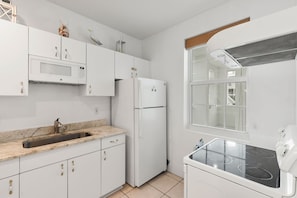Une cuisine moderne avec des meubles blancs, un évier en acier inoxydable, un four à micro-ondes, un réfrigérateur et une cuisinière.