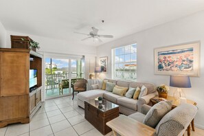 Un salon spacieux avec un grand canapé, une table basse et un téléviseur. Il y a un balcon avec vue sur la ville.