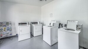 A laundry room with four white washing machines and dryers, a ceiling fan, and a bulletin board with various notices.