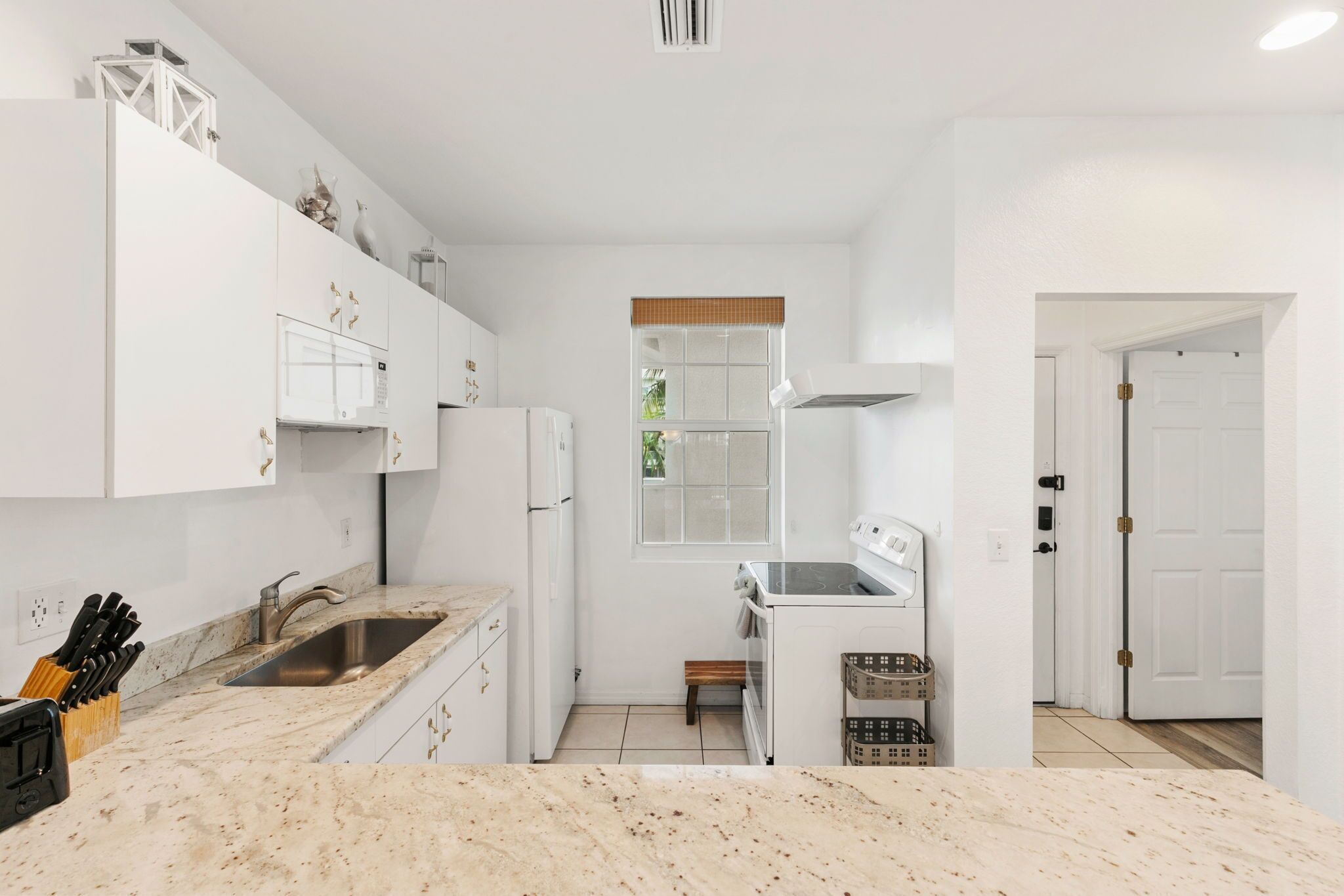 Uma cozinha moderna com armários brancos, bancada de mármore, forno embutido e uma janela com vista.